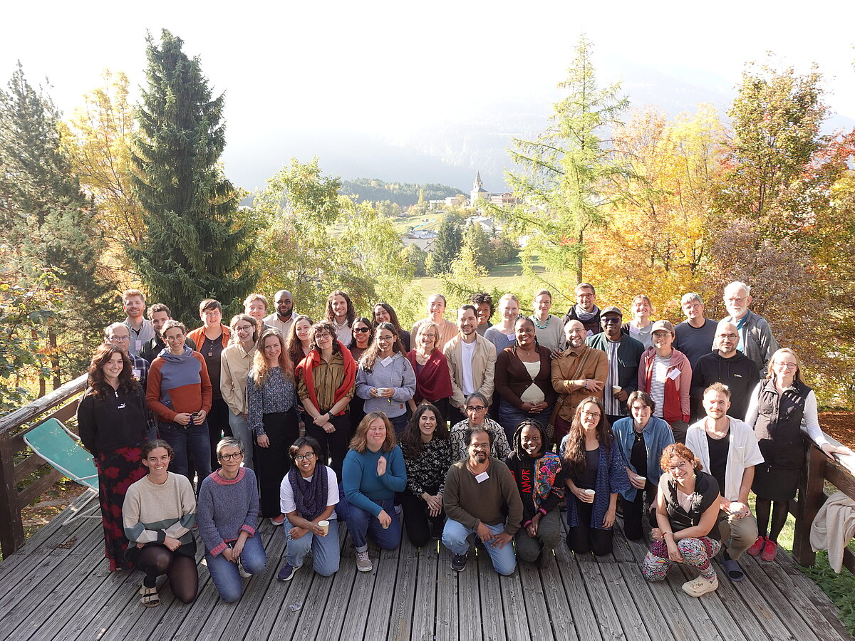 Attēlā redzama vairāk nekā 20 cilvēku grupa, kura izvietojusies uz koka terases. Fonā redzami dažādi koki. Attēlā redzama vairāk nekā 20 cilvēku grupa, kura izvietojusies uz koka terases. Fonā redzami dažādi koki.